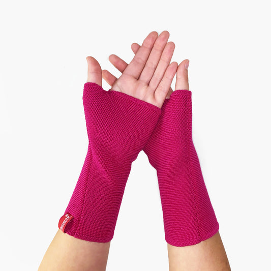 zwei Hände tragen Pinke Armstulpen mit abgenähtem Daumenloch. Man sieht das außenliegende Knötchenmuster. Innen sind die Stulpen Glatt rechts gestrickt.