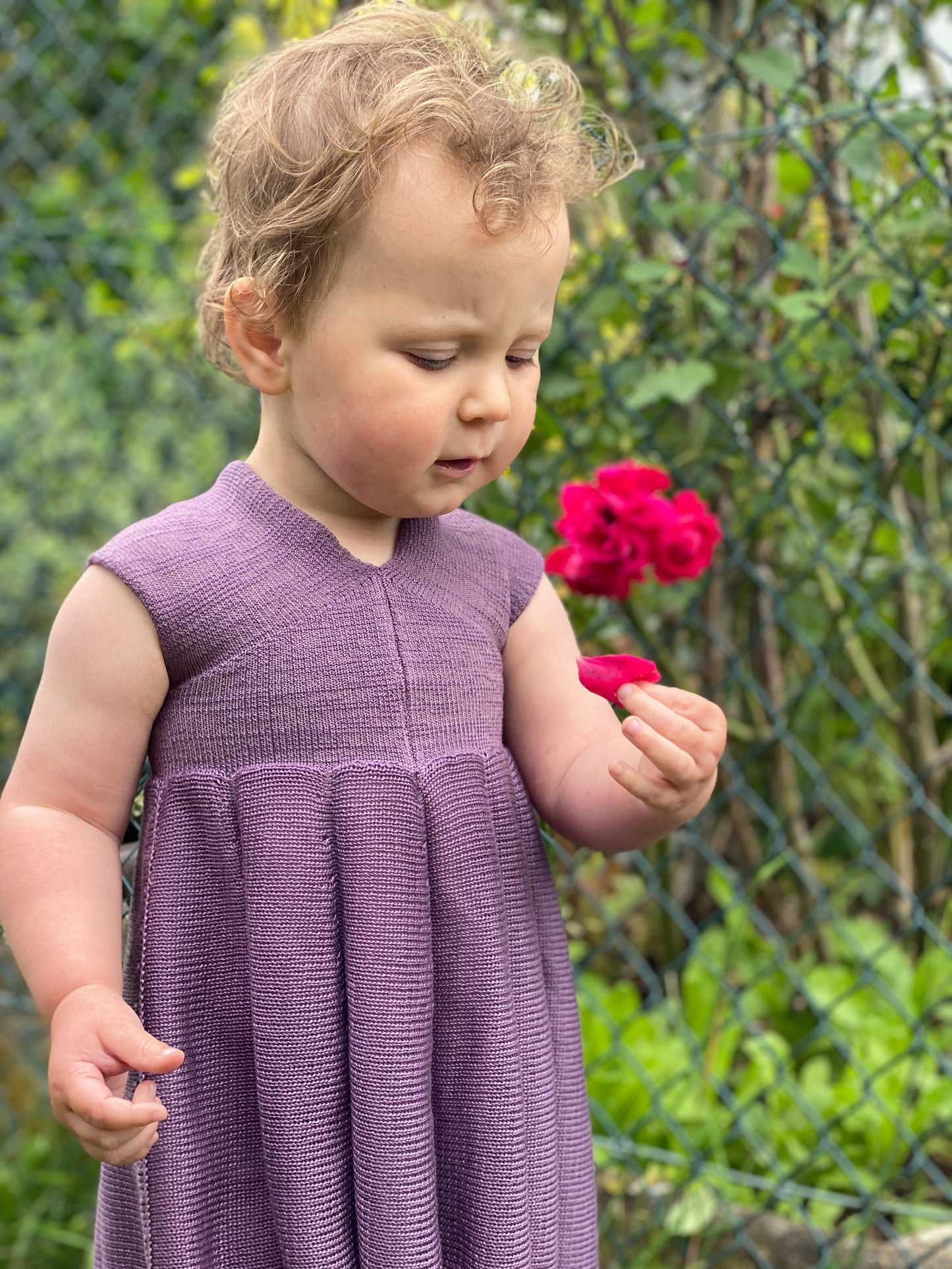 Ein Mädchen mit einer roten Rose in der Hand trägt ein Sommerkleid von vincente aus Tencel/Lyocell gestrickt in Lila