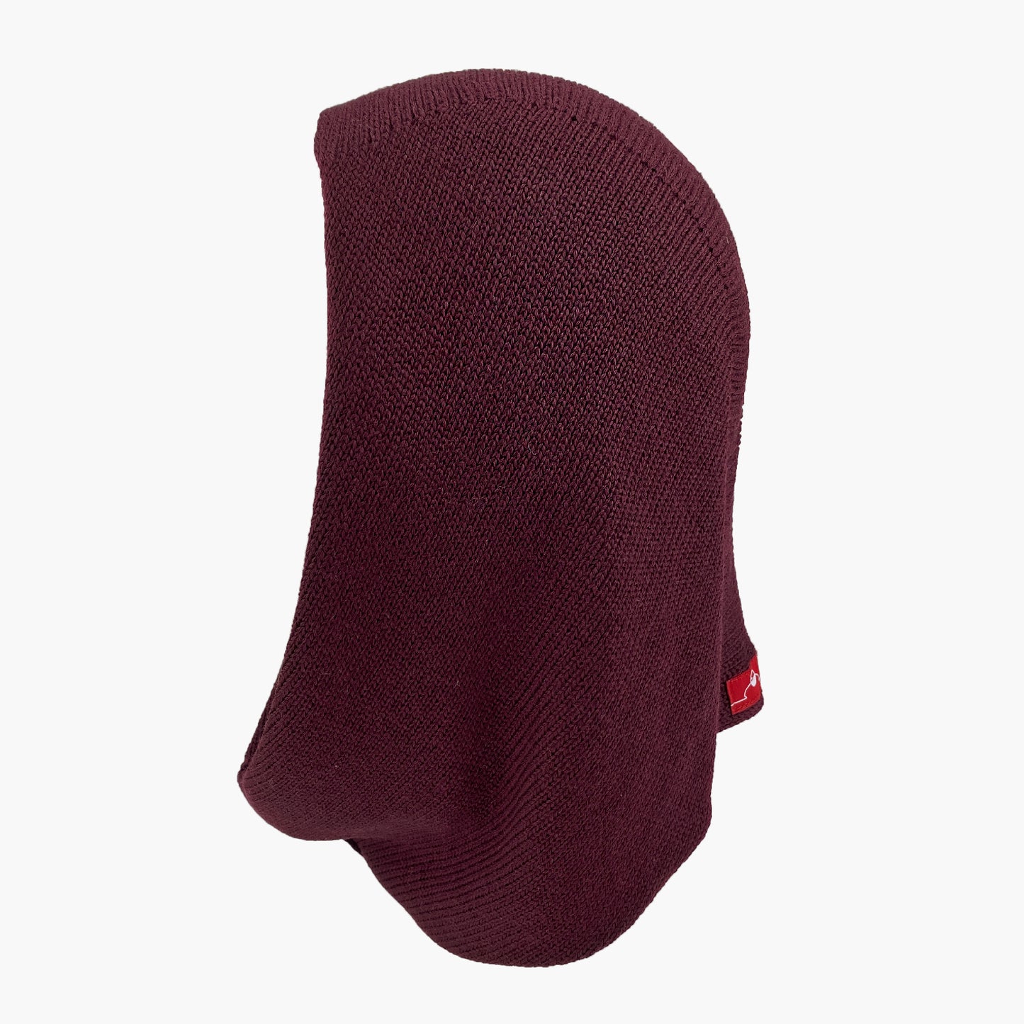 Mütze deren Form den Kopf umspielt, und auch das Kinn bedeckt, ähnlich einer geschlossenen Kapuze. Die Balaclava liegt flach, so daß man diese Kapuzenform: oben breiter zum Hals Schmal zulaufend, gut sehen kann. Sie ist Bordeauxrot und aus Merinowolle gestrickt.