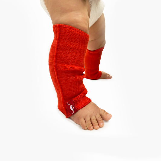 Man sieht ein speckiges Babybein angezogen mit einer Beinstulpen aus Wolle gestrickt in leuchtendem Rot oder Rosso