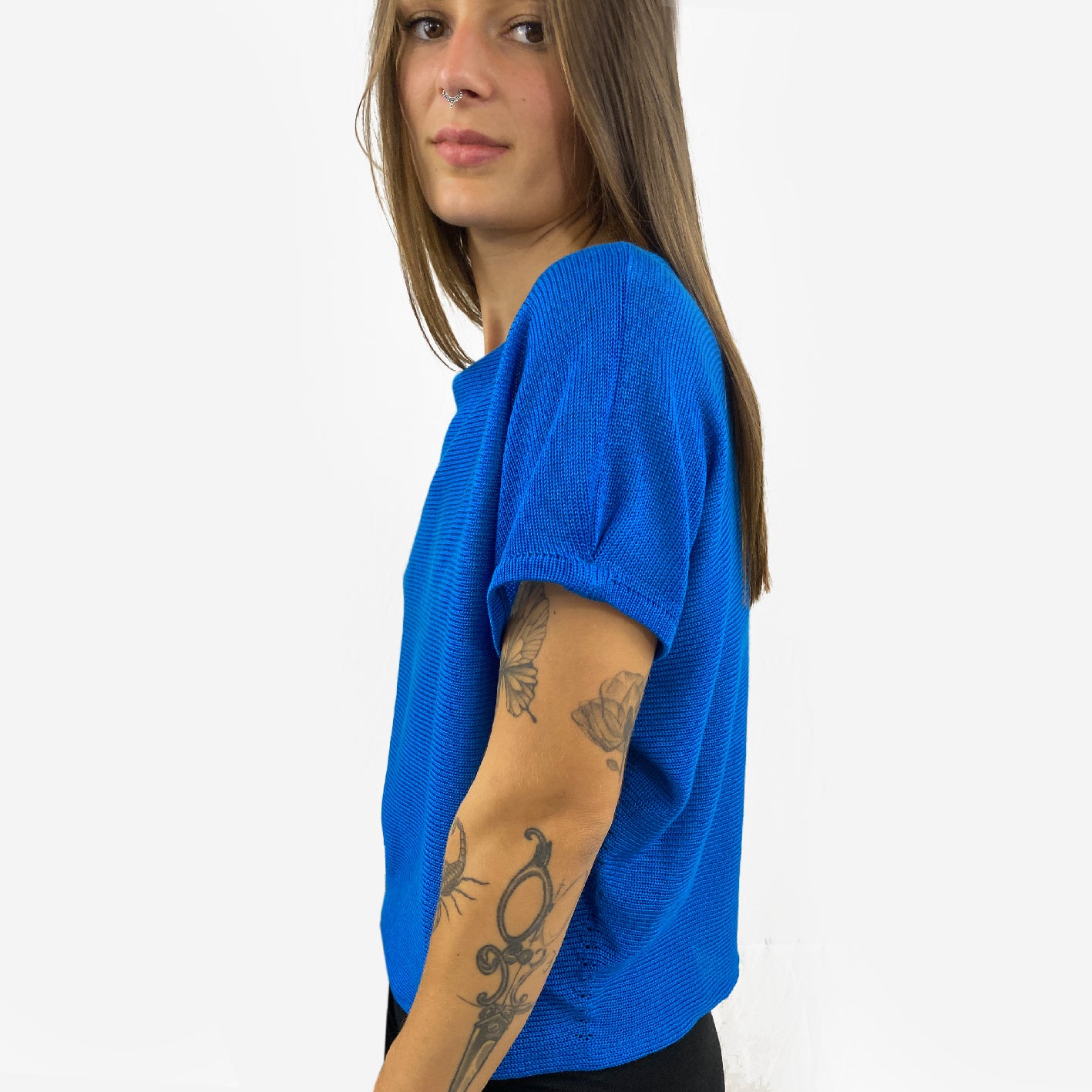 Unser Model mit glatten, Langem, braunem Haar und Taatoos (Schmetterling, Scorpion) auf dem Arm trägt ein seidig gänzendes T-shirt von vincente. Das Shirt ist aus Tencel/Lyocell gestrickt hat eine kleine Falte an dem kurzen Arm und ist leuchtend Blau.