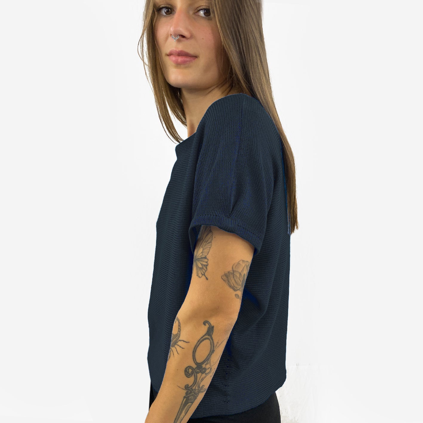 Unser Model mit glatten, Langem, braunem Haar und Taatoos (Schmetterling, Scorpion) auf dem Arm trägt ein seidig gänzendes T-shirt von vincente. Das Shirt ist aus Tencel/Lyocell gestrickt hat eine kleine Falte an dem kurzen Arm und ist Schwarz