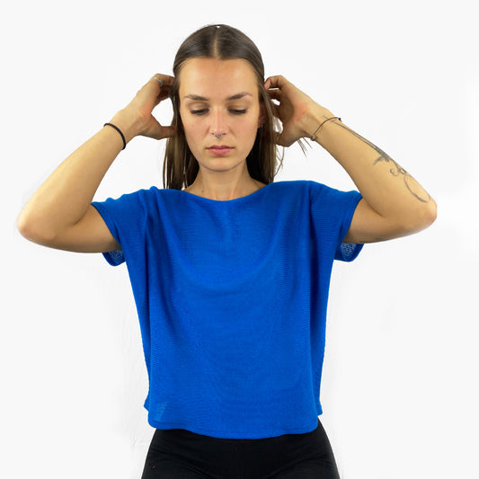 Unser Model mit glatten, Langem, braunem Haar und Taatoos (Schmetterling, Scorpion) auf dem Arm trägt ein seidig gänzendes T-shirt von vincente. Das Shirt ist aus Tencel/Lyocell gestrickt hat eine kleine Falte an dem kurzen Arm und ist leuchtend Blau.