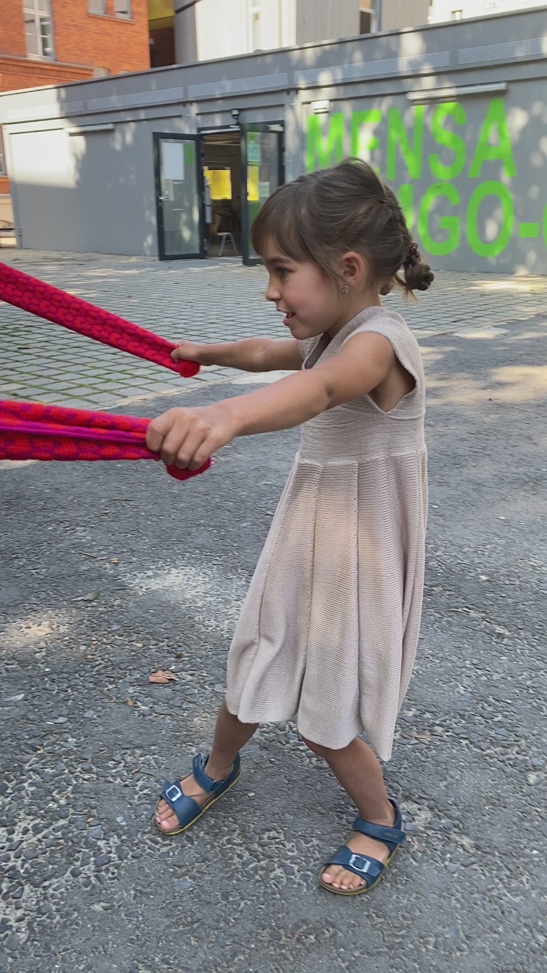 Film mit einem Mädchen, daß  ein Sommerkleid von vincente aus Tencel/Lyocell gestrickt in Beige trägt. Das Mädchen tanzt ausgelassen in einem Schulhof