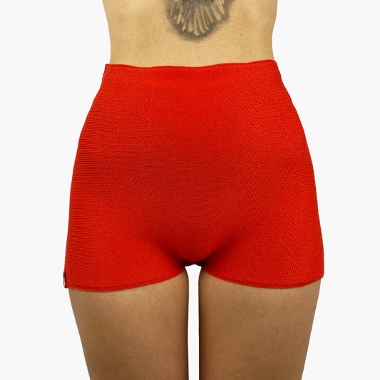 ein Model trägt eine Orangerote Wollunterhose mit angeschnittenem kurzen Bein. Die Hotpants geht bis zur Taille.