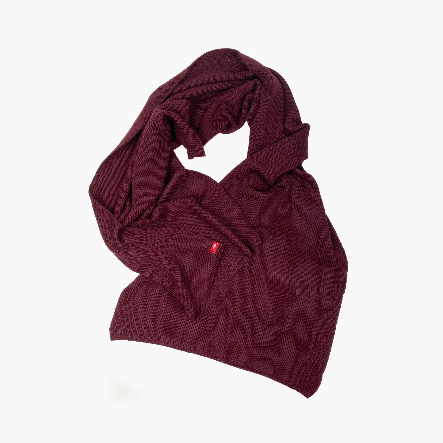 Bordeaux-roter, gestrickter Schal im Fangpatentmuster. Eine Seite sieht glatt rechts gestrickt, die andere Seite sieht aus wie minikleine Muscheln oder Punkte. Der Wollschal ist zu einem Haufen drapiert, so sieht man den weichen Fall.