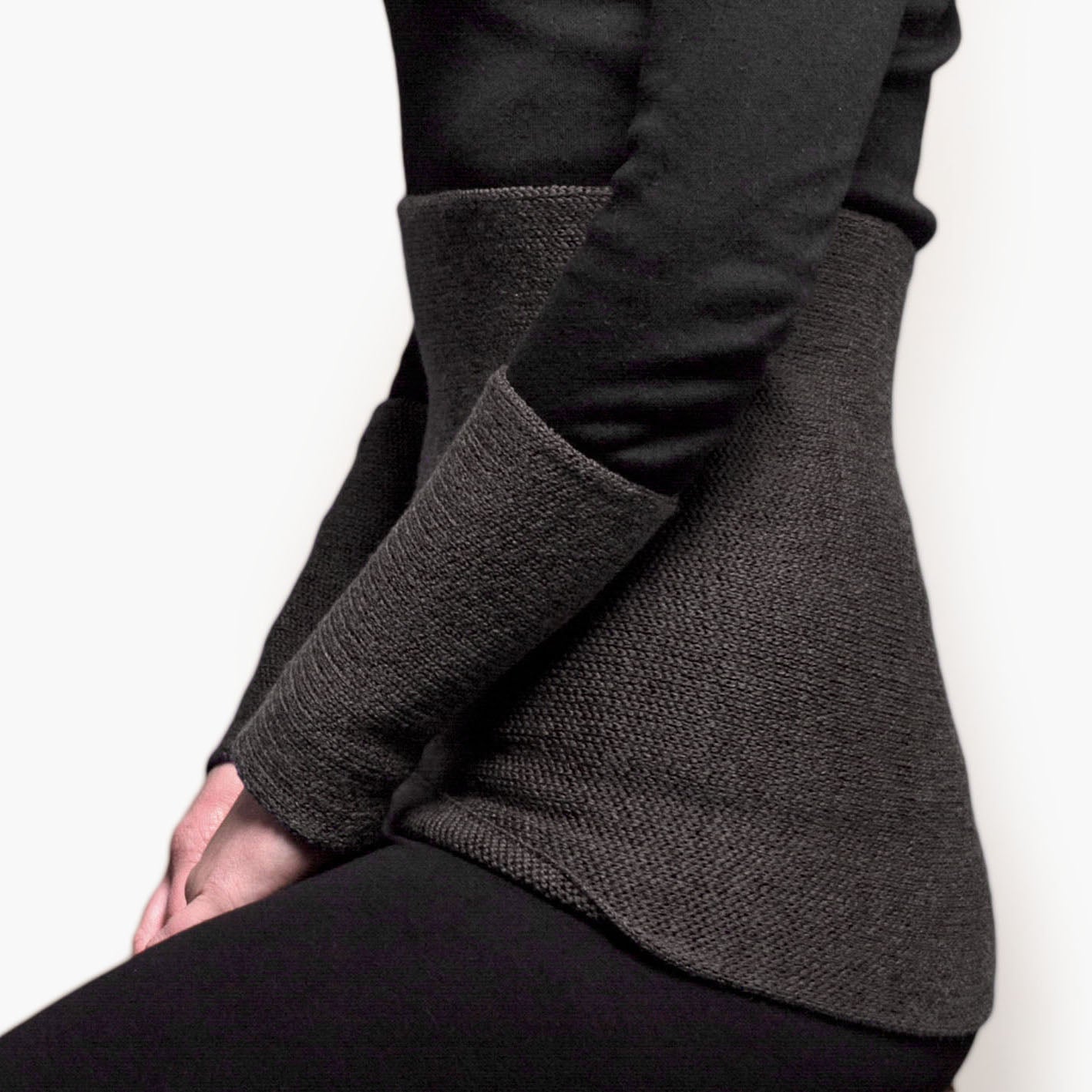 eine Frau ist seitlich zu sehen im Bereich unter der Brust bis zu den Oberschenkeln. Sie trägt einen Nierenwärmer um den Bauch und an den Handgelenken Armstulpen alles in Dunkelgrau.