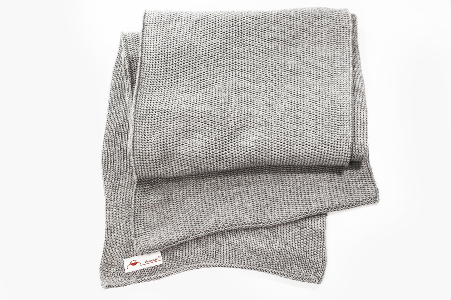 Silbergrauer gestrickter Schal im Fangpatentmuster. Eine Seite sieht glatt rechts gestrickt, die andere Seite sieht aus wie minikleine Muscheln oder Punkte. Der Wollschal ist zu einem Haufen drapiert, so sieht man den weichen Fall