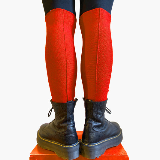 Man sieht ein paar Beine bis zum Knie von Hinten. Sie tragen Orange-rote Beinstulpen von vincente aus Wolle. In der Hinteren Mitte verläuft die Häkelnaht längs. Dazu trägt das Model DocMartens.