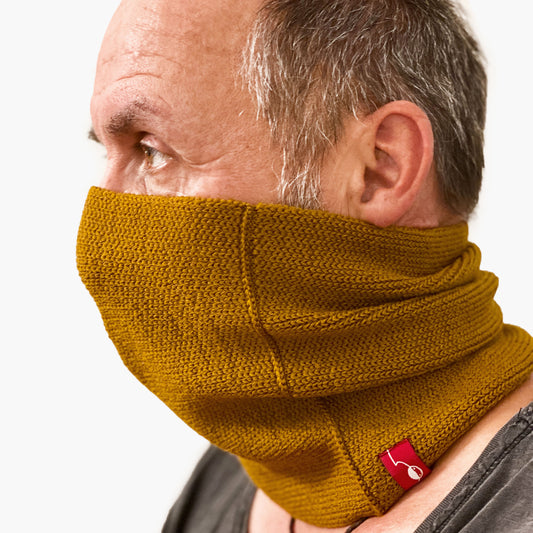 Ein Mann trägt einen Bronce farbenen gestrickten Loop außen glatt rechts gestrick. Er hat den Loop bis über die Nase gezogen.
