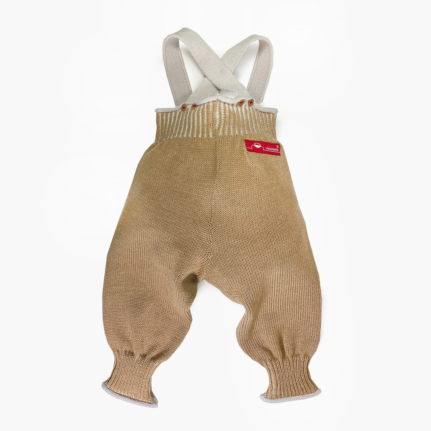 Woll-Hose, Salopette aus Bio-Merinowolle von vincente gestrickt. Sie ist Beige mit Wollweißen Hosenträgern und Streifen im enganliegenden Bündchen. Die Knöpfe sind Beige und mit Roten Garn angenäht