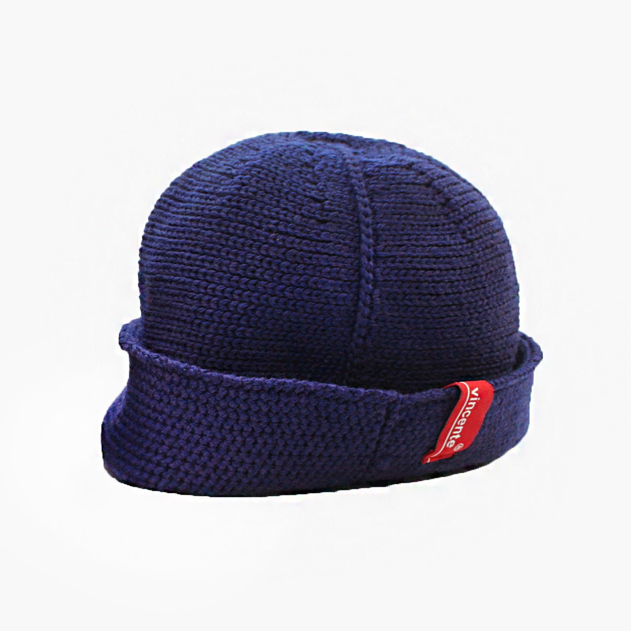Royalblaue Wollmütze aus Merinowolle quer in Kopf-Form gestrickt. Das Fangpatentmuster bedeutet, daß Innen ein Knötchenmuster und außen ein klassiches Rechte Maschenmuster zu sehen ist. Wenn man den Beanie umkrempelt und als Dockermütze trägt ist jeweils das andere Muster zu sehen. Das rote vincente-Label mit der kleinen Ente ist am Rand angenäht. Die Mütze kann insideout getragen werden.