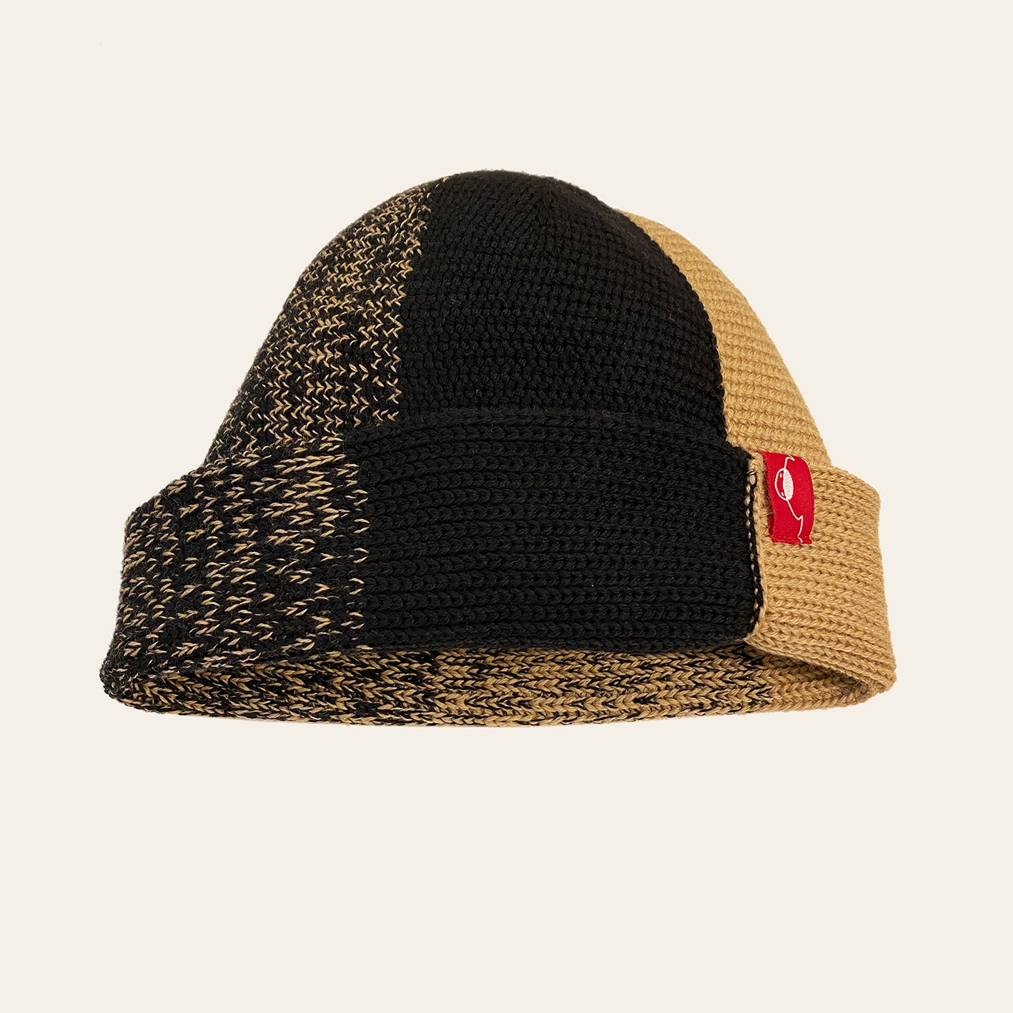 Karamel/Schwarze farbene Beanie. Der Rand ist umgeschlagen, wie bei einer Dockermütze. Die Mütze hat einen Farbverlauf, der sich im Kreis von Karamel mit etwas Schwarz dann etwas mehr Schwarz usw. verhält.