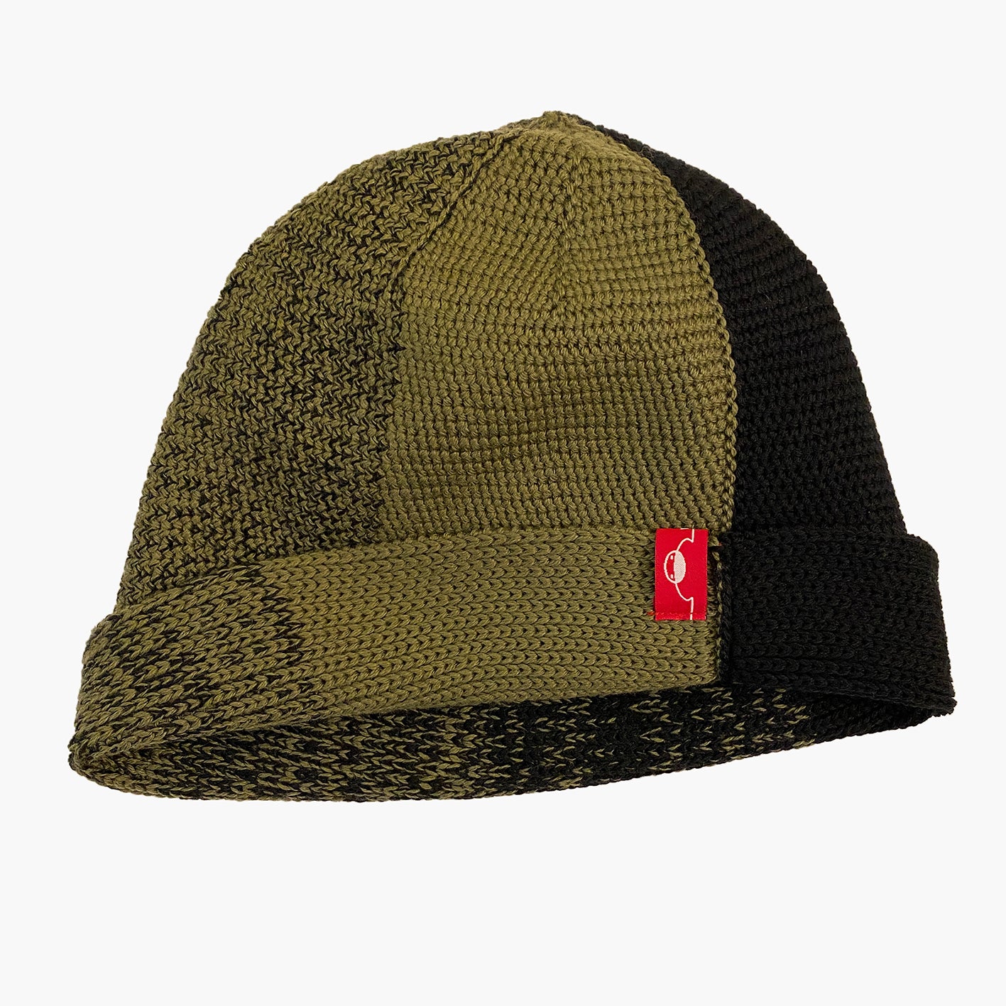 Olive/Schwarze Beanie. Der Rand ist umgeschlagen, wie bei einer Dockermütze. Die Mütze hat einen Farbverlauf, der sich im Kreis wie Tortenstücke verhält. Ein Stück ist Olive-farben ein Stück Schwarz. Dazwischen michen sich die beiden Farben im Farbverlauf von Olive mit etwas Schwarz dann etwas mehr Schwarz usw.
