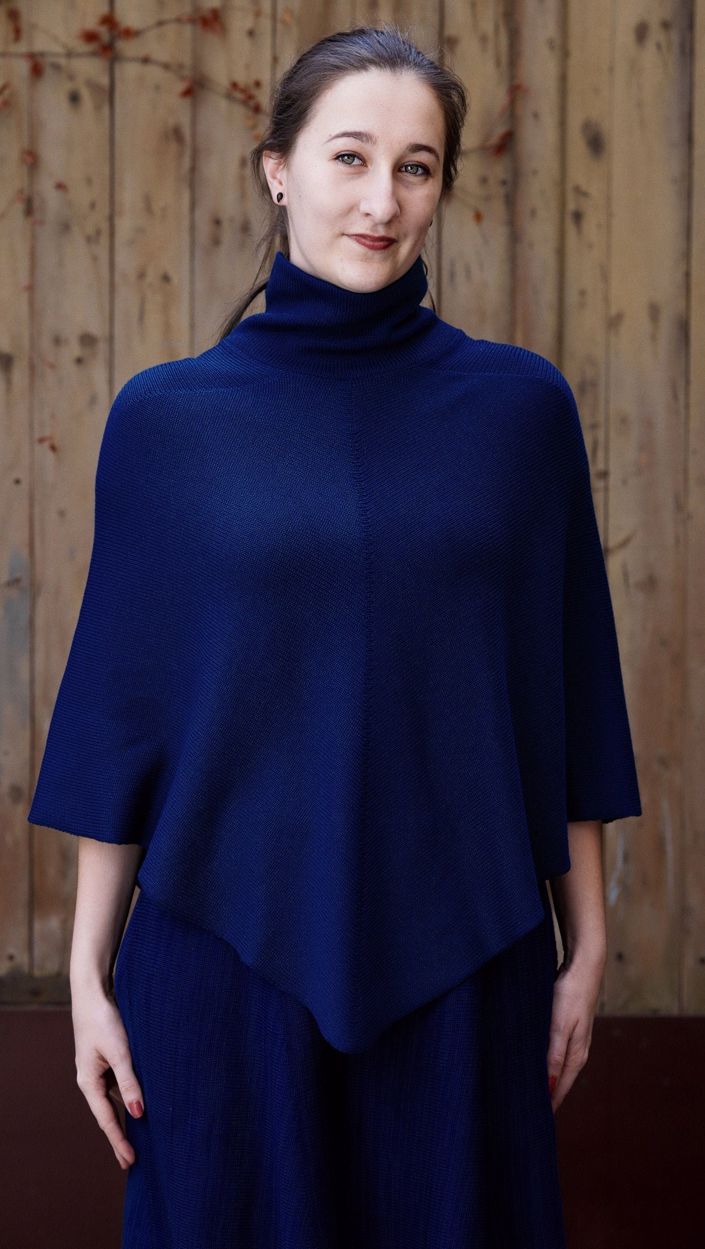 Eine Junge Frau trägt ein royalblaues, gestricktes Cape mit Rollkragen