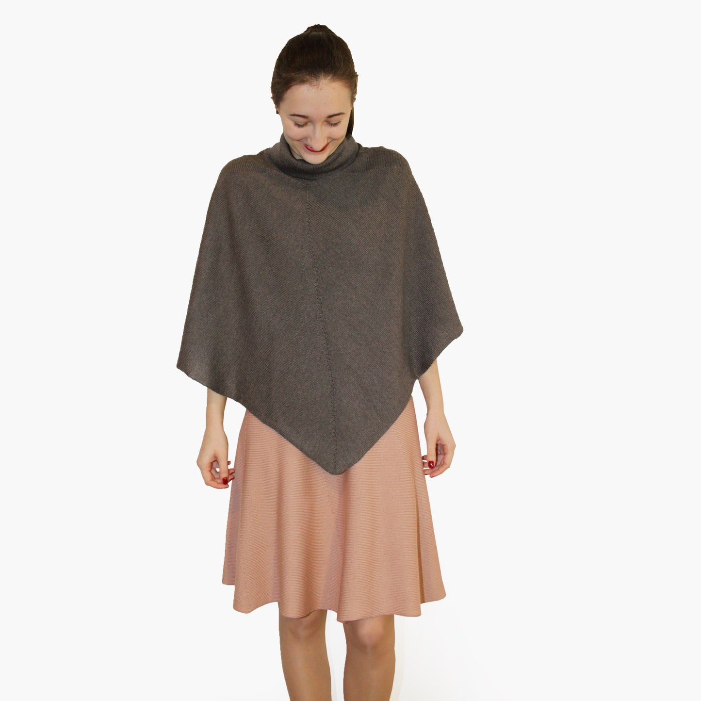Eine junge Frau mit Pferdeschwant trägt ein gestricktes, graues Cape mit Rollkragen und einen rosanen Strickrock