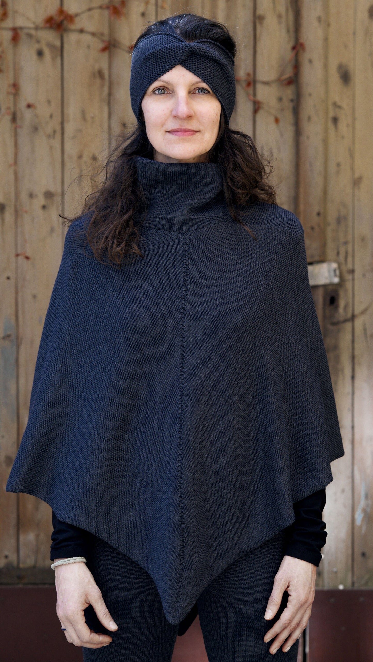 Eine Junge Frau trägt ein dunkelgraues, gestricktes Cape mit Rollkragen