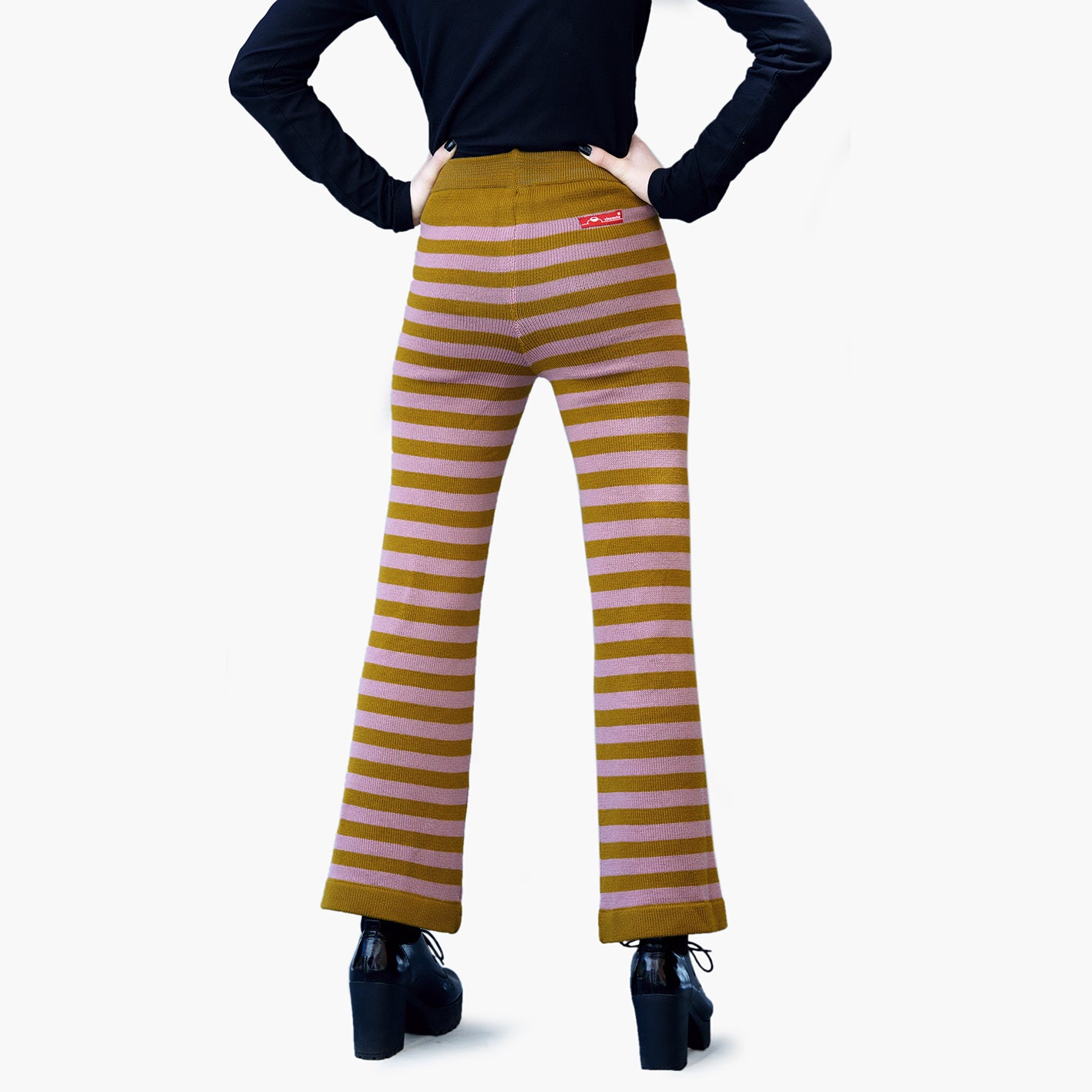 Rückseite einer Jungen Frau in schwarzen Plateauxschuhen, sie trägt eine Gestreife Wollhose. Die Hose hat ca 3cm breite Ringel in Bronce und Rosenholz. Man Sieht Sie von der TAille abwärts.