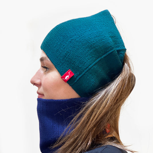 Eine Junge Frau trägt 2 gestrickte Loops, einen in Petrol als Stirnband und einen in Royalblau als Halsschlauch. Das Rote/Weiße vincente-Label ist angenäht.