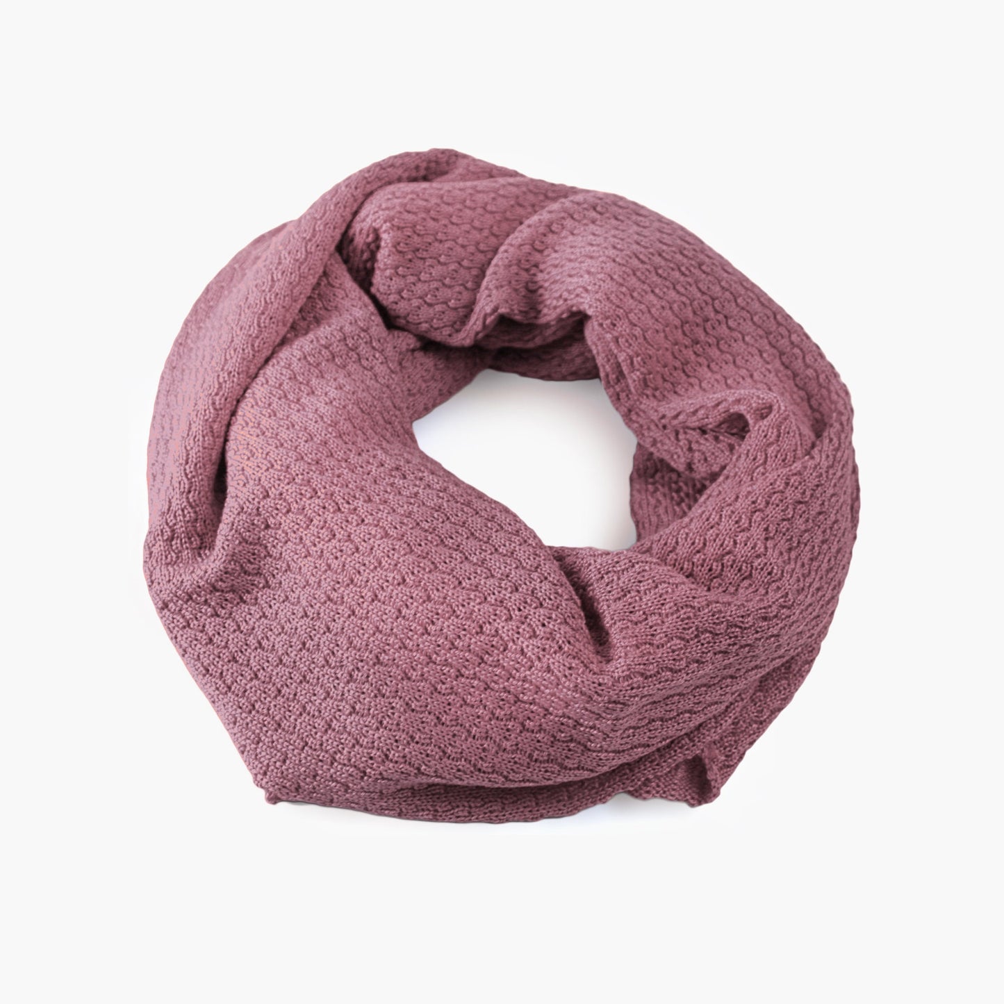 Rosenholz Farbener, gestrickter Loop im Fangpatentmuster. Eine Seite sieht glatt rechts mit kleinen Wellen gestrickt aus, die andere Seite sieht aus wie kleine Muscheln. Der Wollschal ist zu einem Haufen drapiert, so sieht man den weichen Fall.