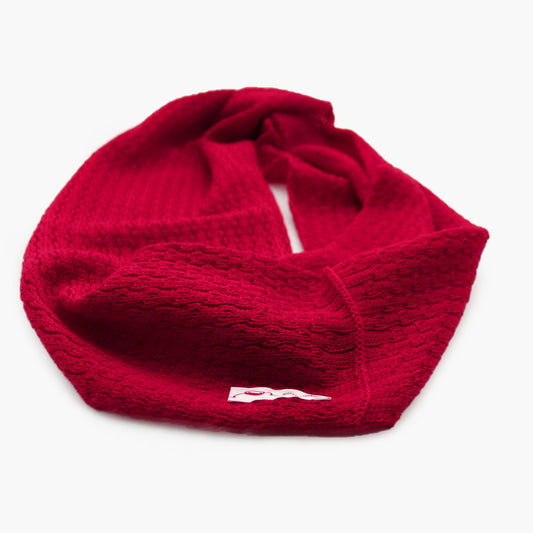 Roter, gestrickter Loop im Fangpatentmuster. Eine Seite sieht glatt rechts mit kleinen Wellen gestrickt aus, die andere Seite sieht aus wie kleine Muscheln. Der Wollschal ist zu einem Haufen drapiert, so sieht man den weichen Fall.