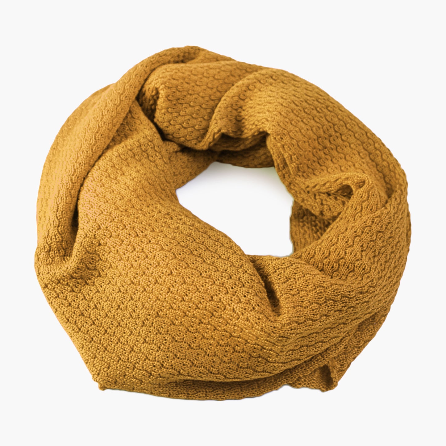 Goldfarbener, gestrickter Loop im Fangpatentmuster. Eine Seite sieht glatt rechts mit kleinen Wellen gestrickt aus, die andere Seite sieht aus wie kleine Muscheln. Der Wollschal ist zu einem Haufen drapiert, so sieht man den weichen Fall.