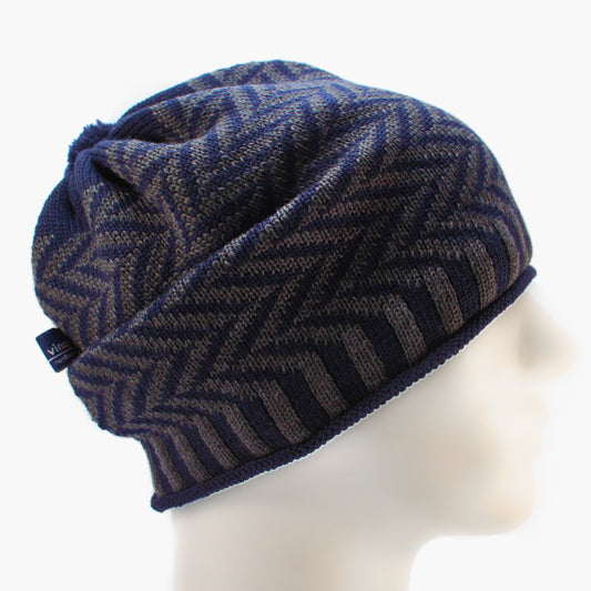 Grau/Royalblaue Beanie-Mütze aus Merinowolle mit längs gestreiften elastischem Bündchen. Die Mütze ist im klassichem Fischgrätmuster gestrickt und hat eine kleine unauffällige Bommel.