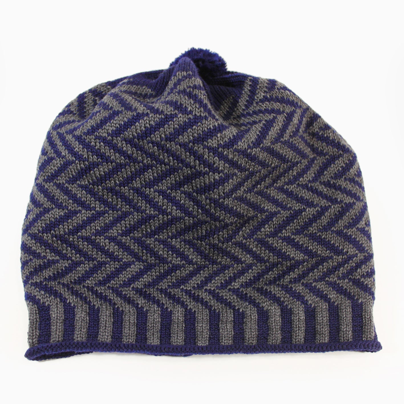 Grau/Royalblaue Beanie-Mütze aus Merinowolle mit längs gestreiften elastischem Bündchen. Die Mütze ist im klassichem Fischgrätmuster gestrickt und hat eine kleine unauffällige Bommel.