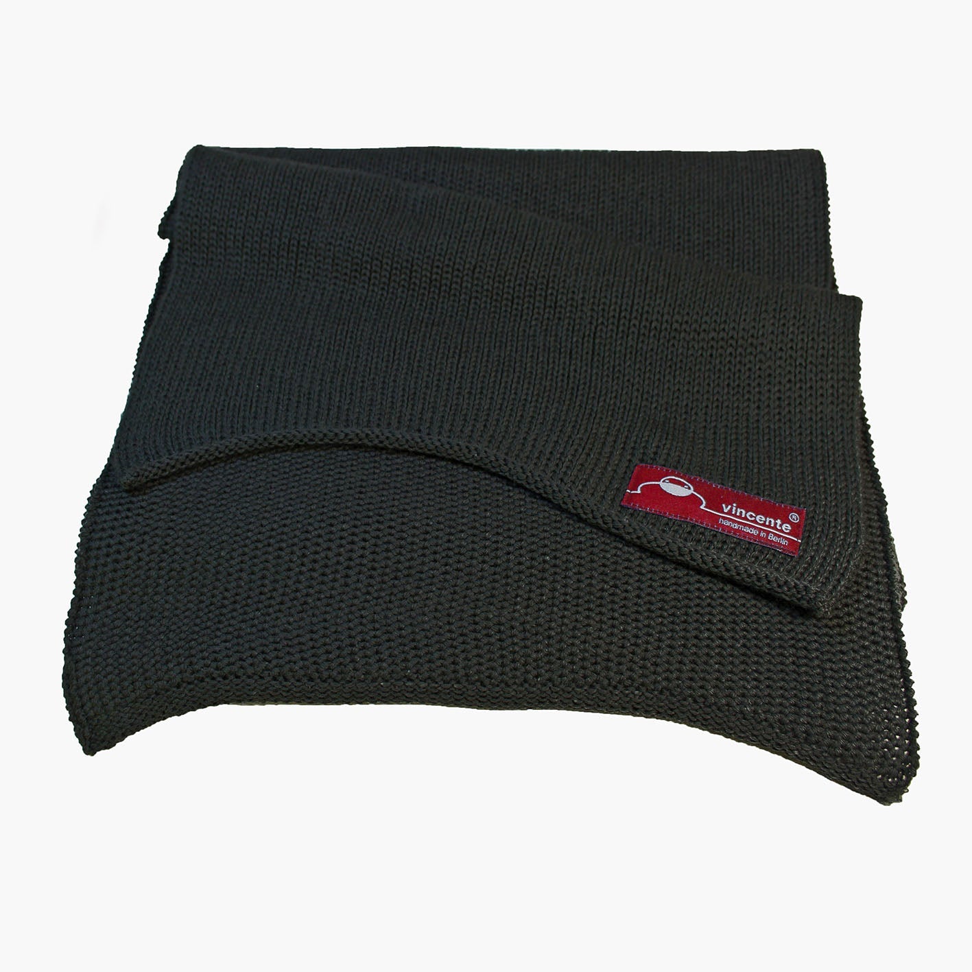 Schwarzer, gestrickter Schal im Fangpatentmuster. Eine Seite sieht glatt rechts gestrickt, die andere Seite sieht aus wie minikleine Muscheln oder Punkte. Der Wollschal ist zu einem Haufen drapiert, so sieht man den weichen Fall.