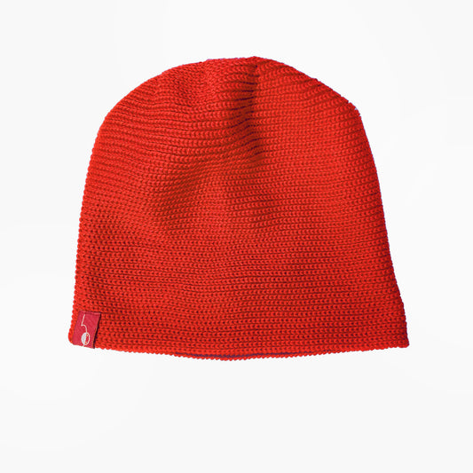 Orange-Rote Beanie-Mütze aus Merinowolle quer in Kopf-Form gestrickt. Das Fangpatenmuster bedeutet daß Innen ein Knötchenmuster und außen ein klasiches Rechte Maschenmuster zu sehen ist. Das rote vincente-Label mit der kleinen Ente ist am Rand angenäht. 