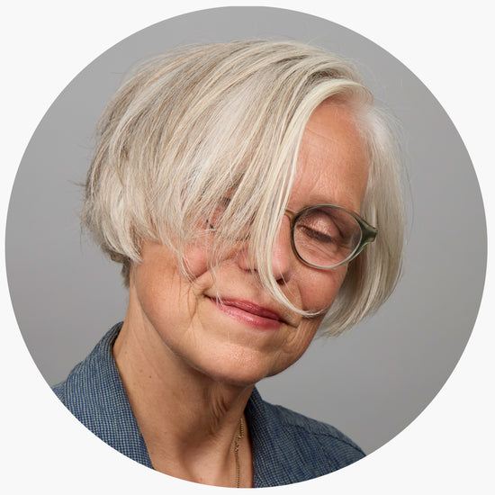 Portrait einer Frau mit Silbergrauen Haaren, die das halbe Gesicht verdecken. Die Frau lächelt zufrieden mit  geschlossenen Augen