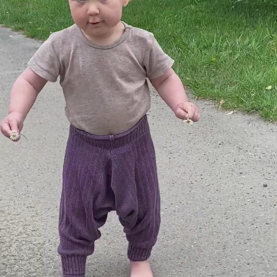 Ein Baby trägt eine Lila Sarouelhose von vincente und tanz dabei auf einer Straße