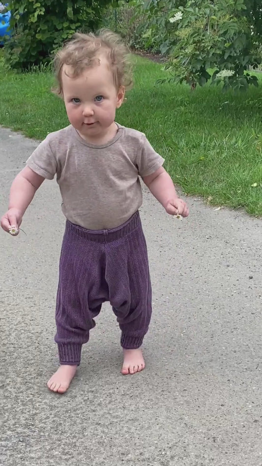 Ein Baby trägt eine Lila Sarouelhose von vincente und tanz dabei auf einer Straße