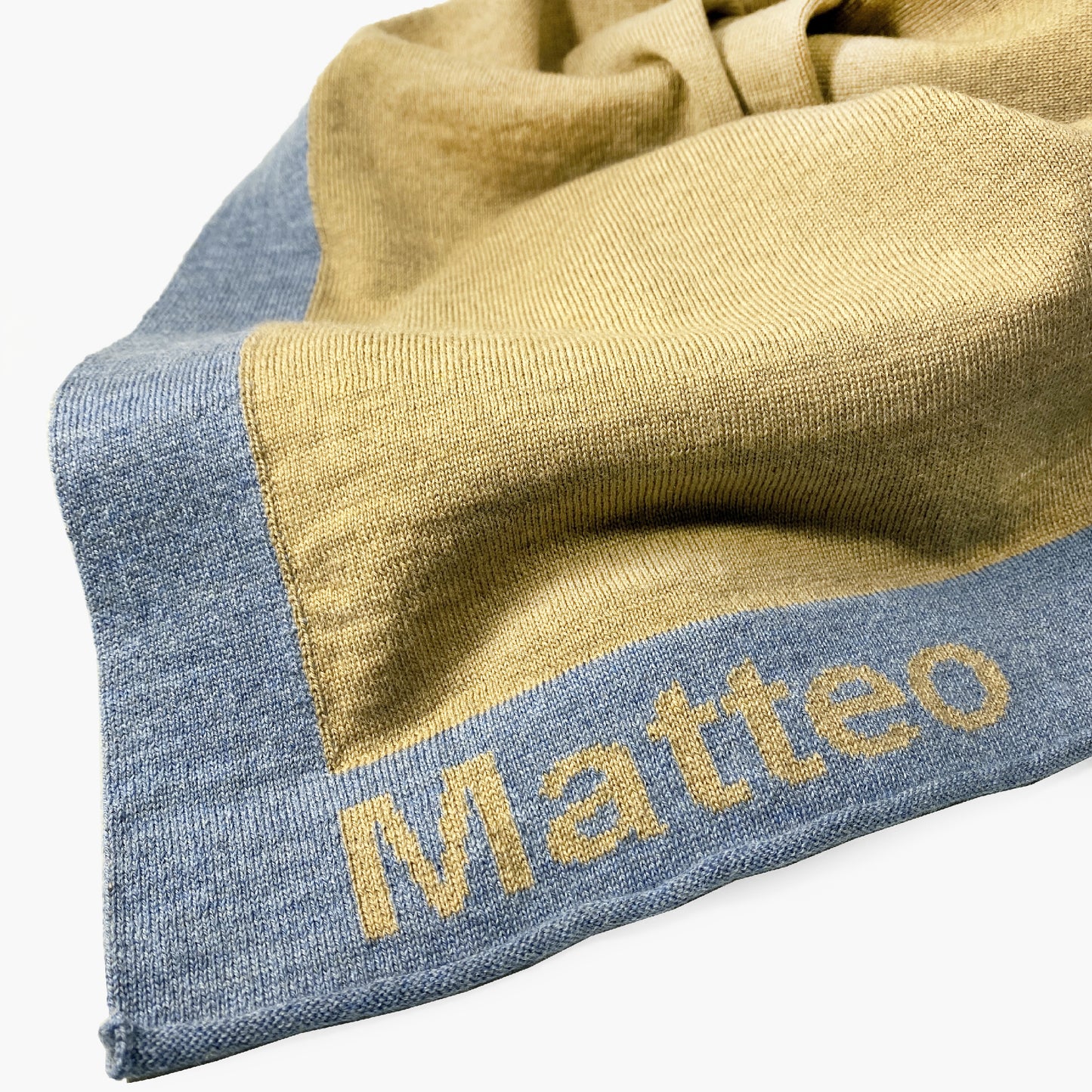 Man sieht die Ecke einer Karamelfarbenen Babydecke. Der Rand ist mit dem Namen Matteo bestickt.
