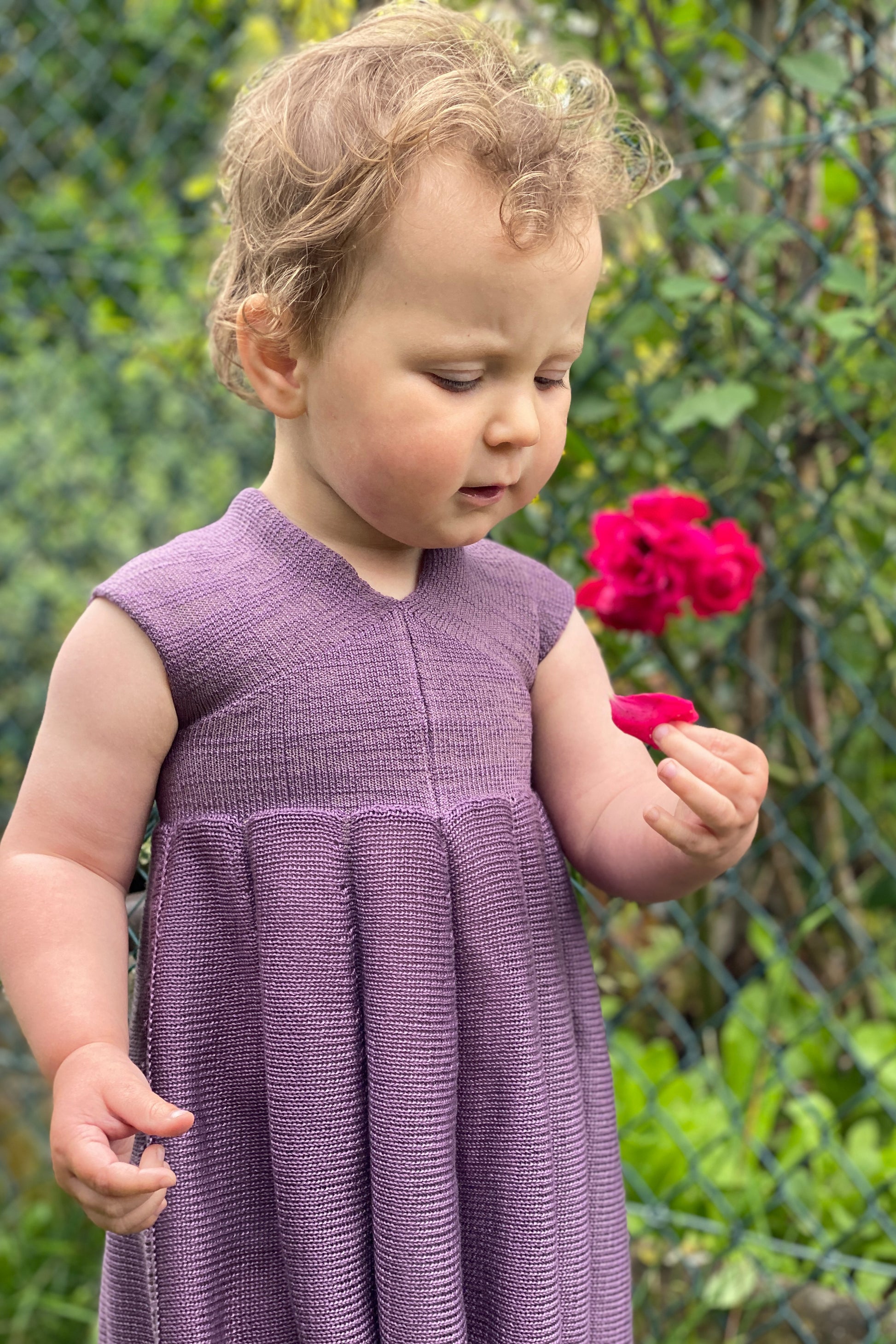 Ein Mädchen mit einer roten Rose in der Hand, trägt ein Sommerkleid von vincente aus Tencel/Lyocell gestrickt in Lila