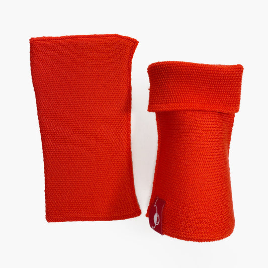 Orangerote, aufrecht stehende Armstulpen. Man sieht das außenliegende Glatt Rechts Muster. Innen sind die Stulpen in einem Feinen Knötchenmuster gestrickt, man kann sie auch Innsideout tragen