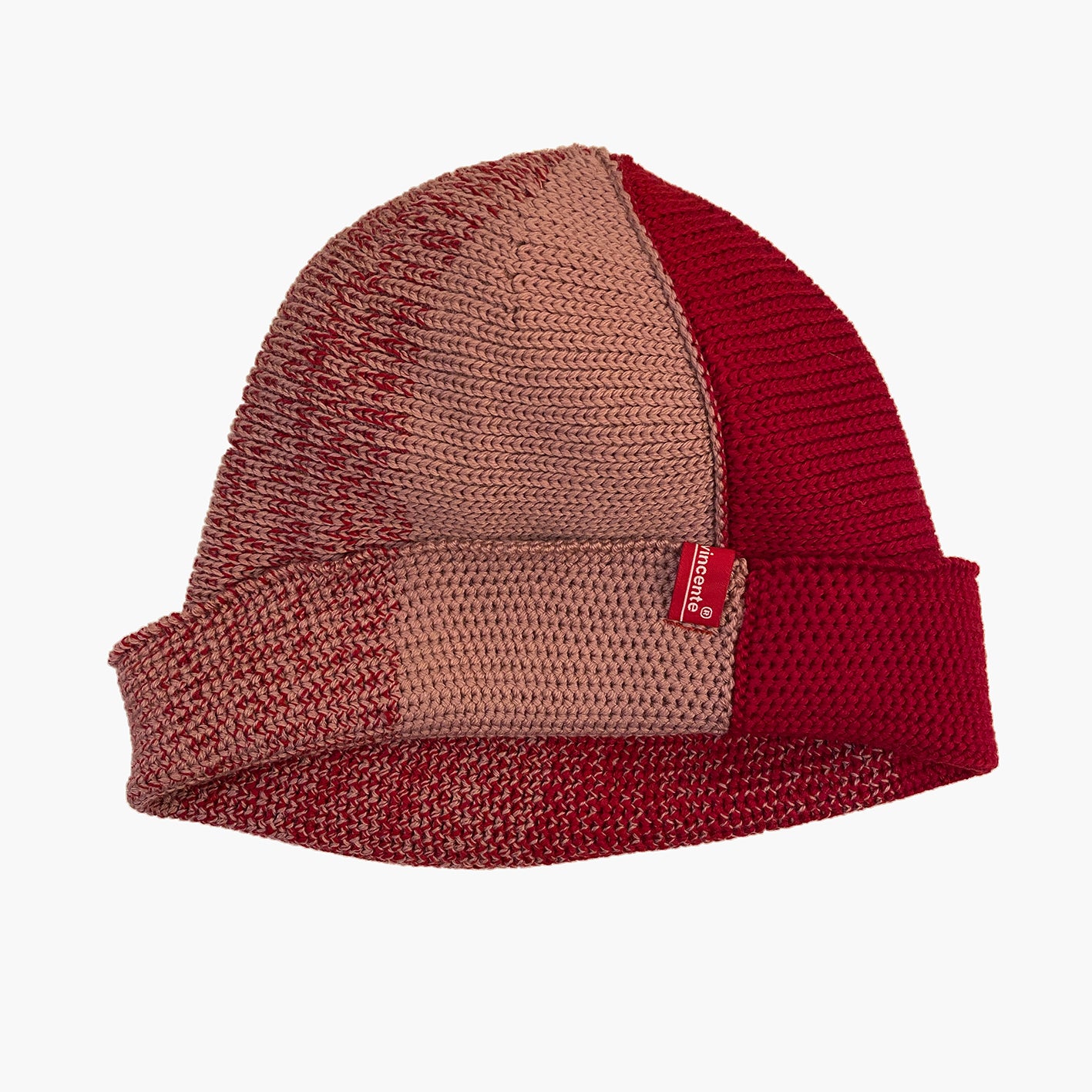 Rot/Rosenholz farbene Beanie. Der Rand ist umgeschlagen, wie bei einer Dockermütze. So sieht man das Innere  Knötchenmuster, wärend die Mütze außen rechtsgestrickt erscheint. Die Mütze hat einen Farbverlauf, der sich im Kreis wie Tortenstücke verhält. Ein Stück ist Rosenholz-farben ein Stück Rot. Dazwischen  michen sich die beiden Farben im Farbverlauf von Rosa mit etwas Rot dann etwas mehr Rot usw.