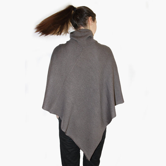 Die Rückseite einer Jungen Frau. Ihr Pferdeschwanz schwingt durch die Luft. Sie trägt ein Graues, gestricktes Cape mit Rollkragen