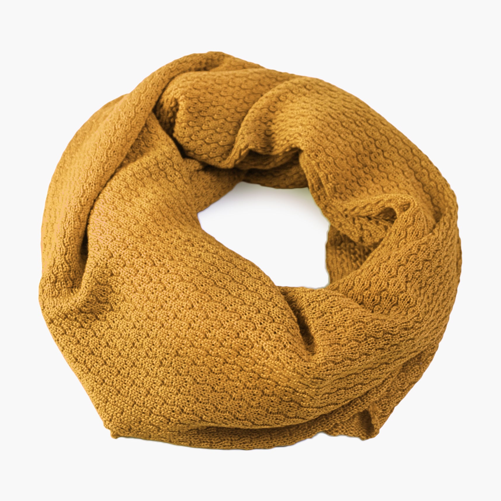 Goldfarbener, gestrickter Loop im Fangpatentmuster. Eine Seite sieht glatt rechts mit kleinen Wellen gestrickt aus, die andere Seite sieht aus wie kleine Muscheln. Der Wollschal ist zu einem Haufen drapiert, so sieht man den weichen Fall.